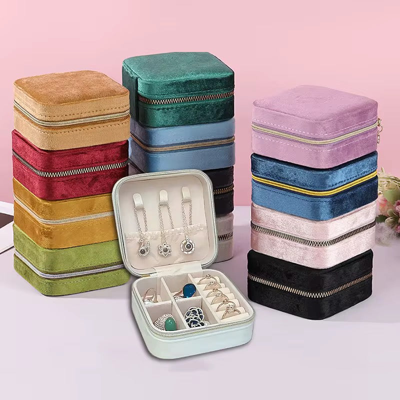 Stacked colorful jewelry boxes with an open one displaying earrings and rings on a light pink background.